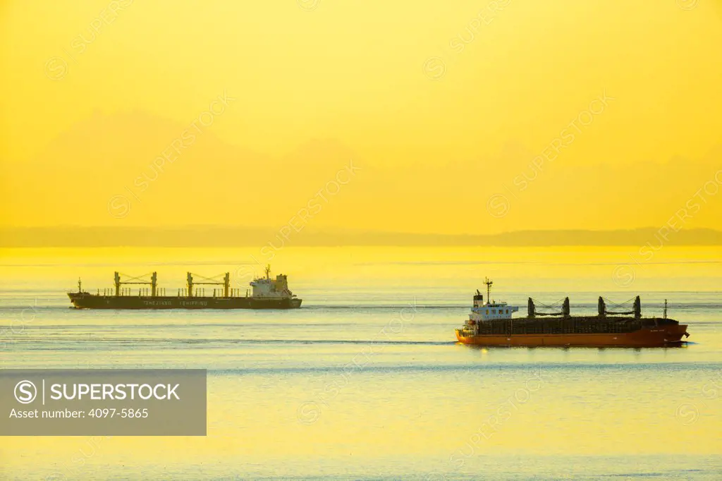 Canada, British Columbia, Vancouver Island, Freighter in Stait of Jaun de Fuca with San Juan Islands in distance at dawn