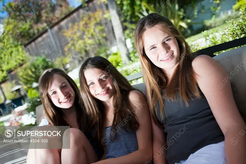 Three teenage girls sitting on a bench and smiling