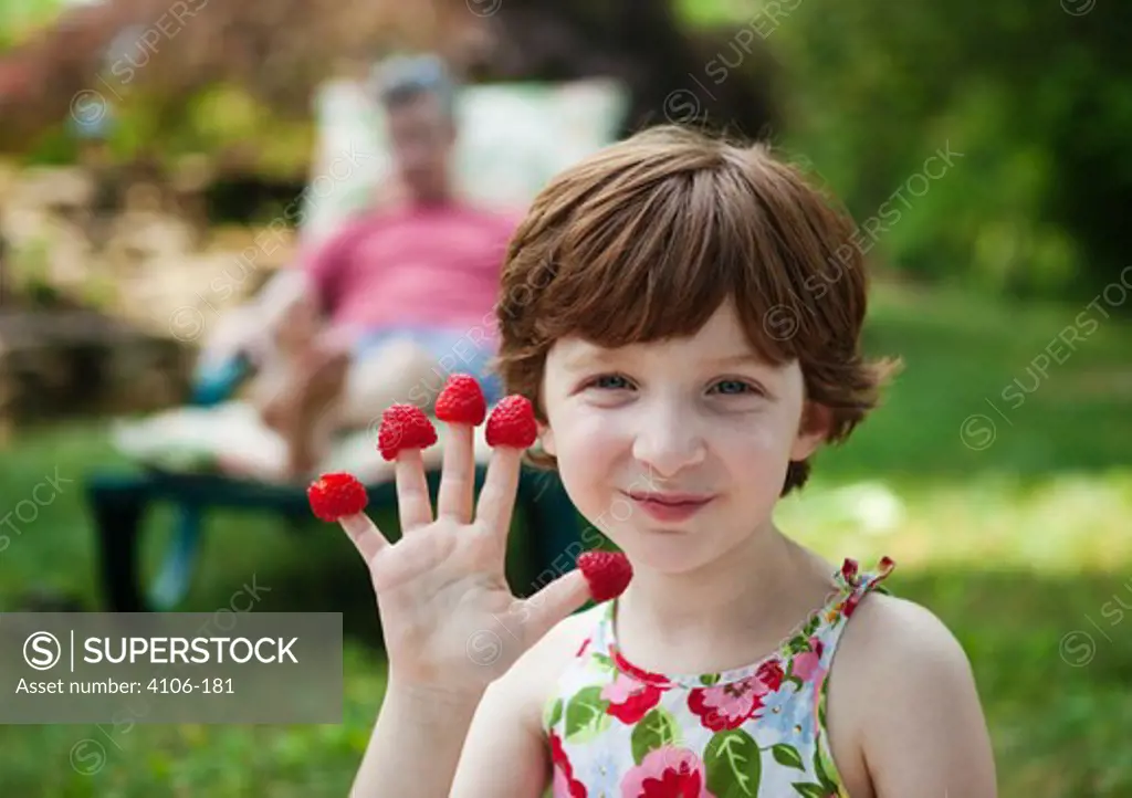 Portrait of girl with raspberries on fingers outdoors
