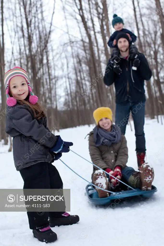 Girl pulling a woman in a sled and boy on his father's shoulders in the snow, Traverse City, Grand Traverse County, Michigan, USA