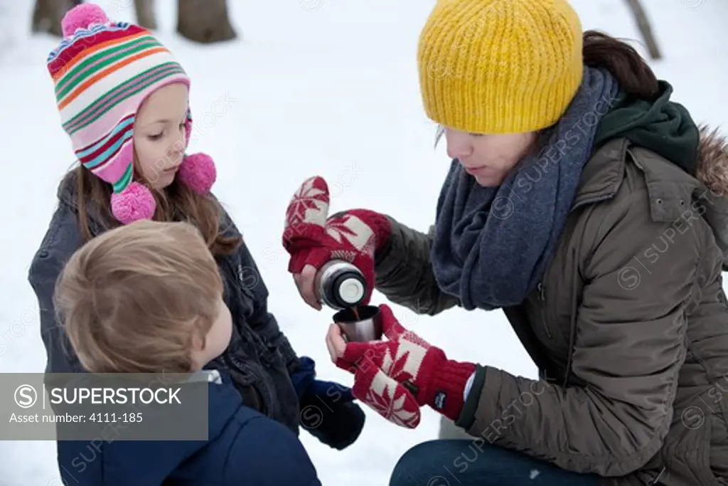 Woman pouring hot chocolate for her children in the snow, Traverse City, Grand Traverse County, Michigan, USA