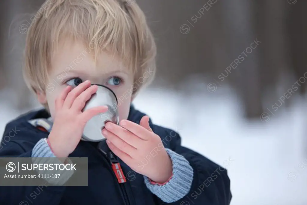 Boy drinking hot chocolate in snow, Traverse City, Grand Traverse County, Michigan, USA