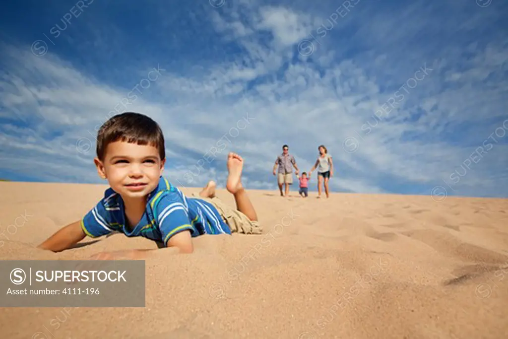 Boy lying in sand with family in the background, Sleeping Bear Dunes National Lakeshore, Glen Arbor, Leelanau County, Michigan, USA