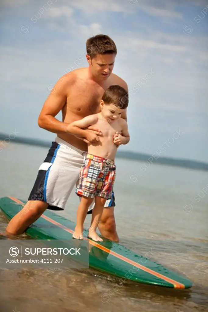 Man helping his son standing on a surfboard, Lake Michigan, Glen Arbor, Leelanau County, Michigan, USA
