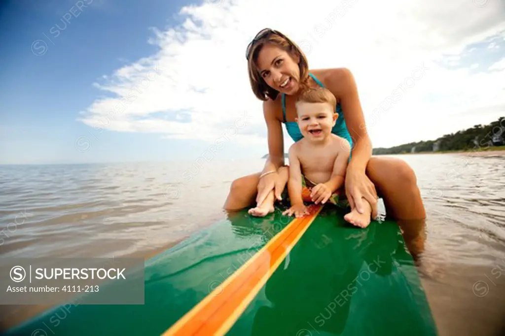 Woman with her baby boy sitting on a surfboard, Lake Michigan, Glen Arbor, Leelanau County, Michigan, USA