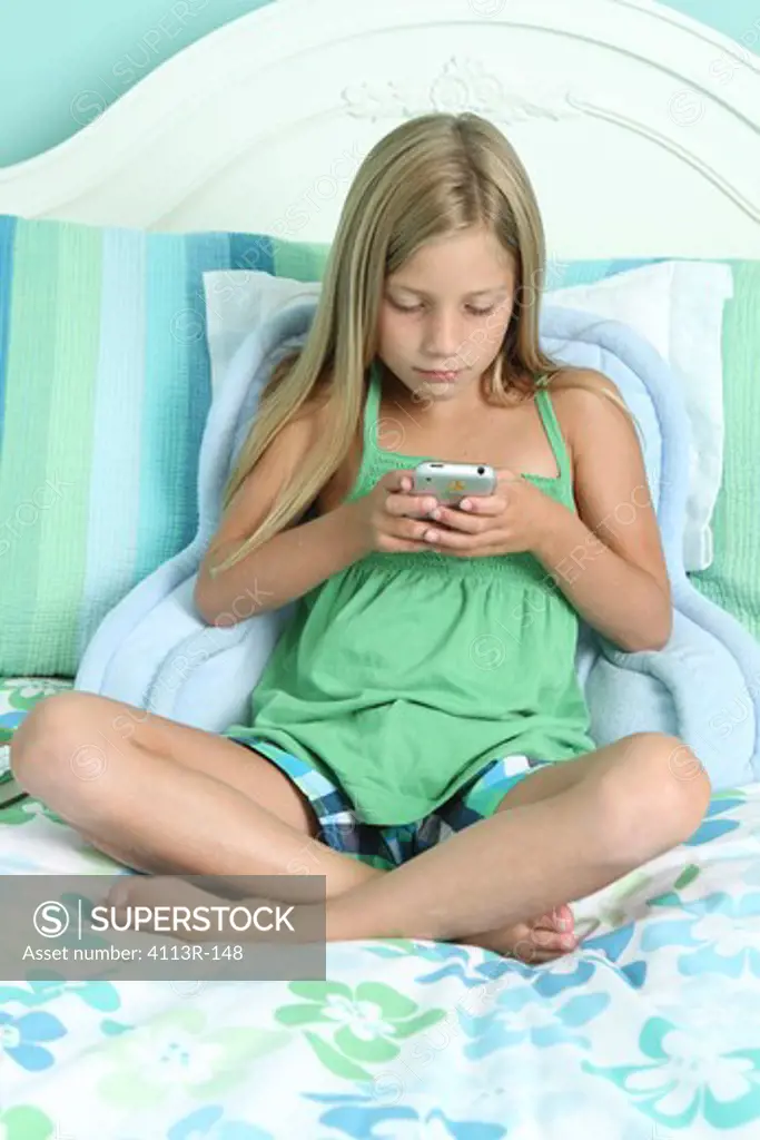 Girl sitting on the bed and text messaging on a mobile phone