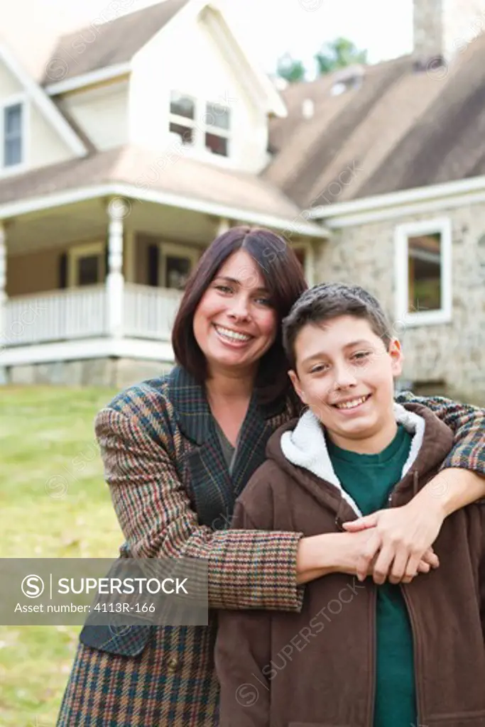 Portrait of smiling mother and son standing in front of large house