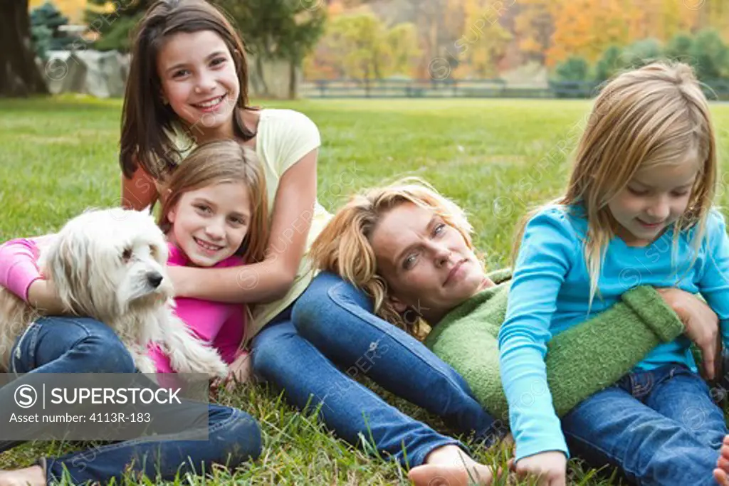 Mother with three daughters and dog relaxing on grass
