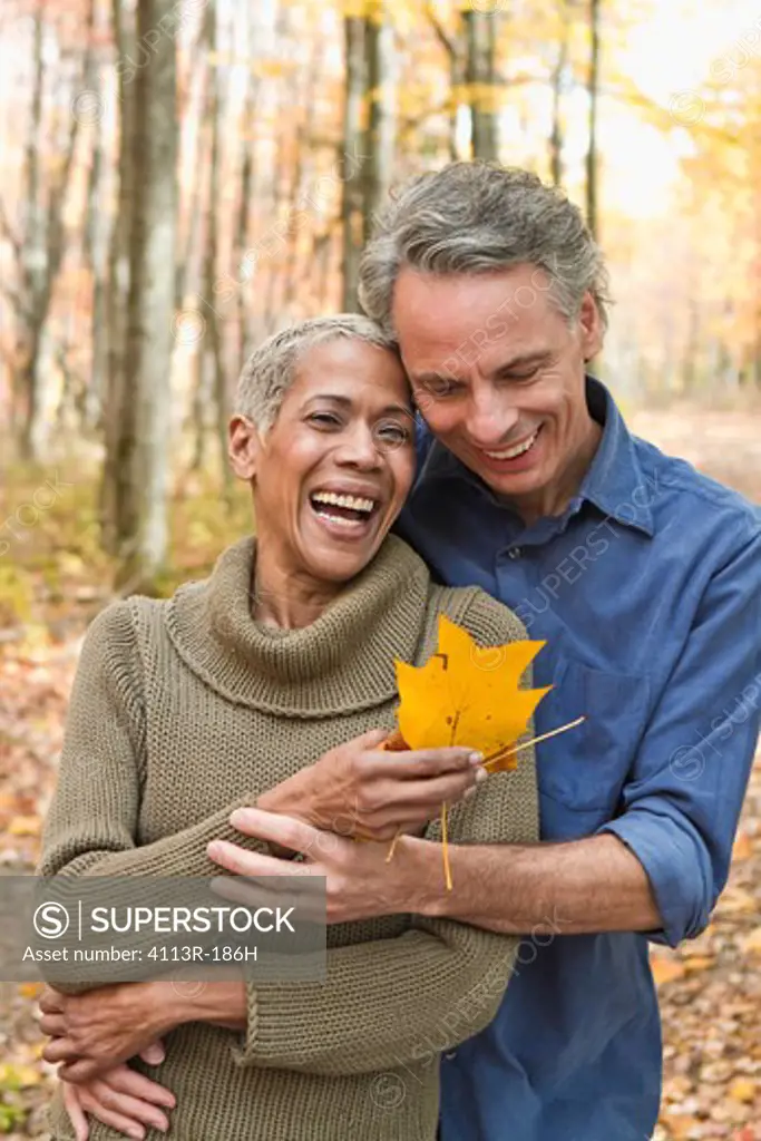Mature couple holding Autumn leaves in forest