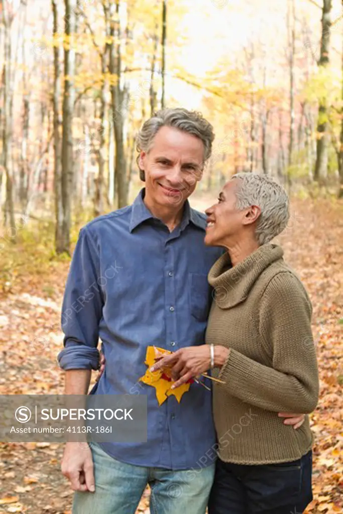 Mature couple holding Autumn leaves in forest