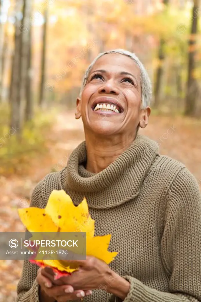 Portrait of mature woman holding Autumn leaves and laughing