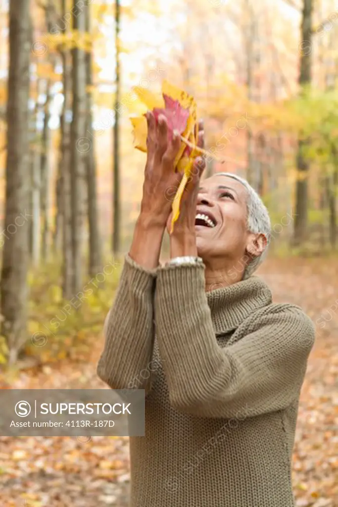 Portrait of mature woman holding Autumn leaves and laughing