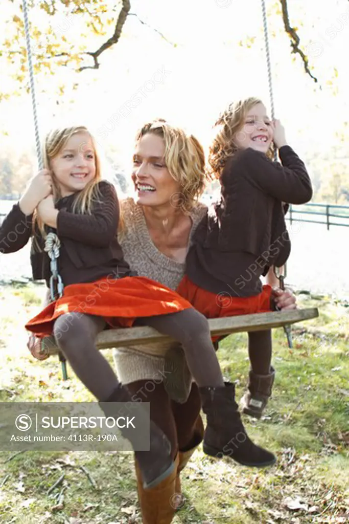 Mother pushing two daughters on swing