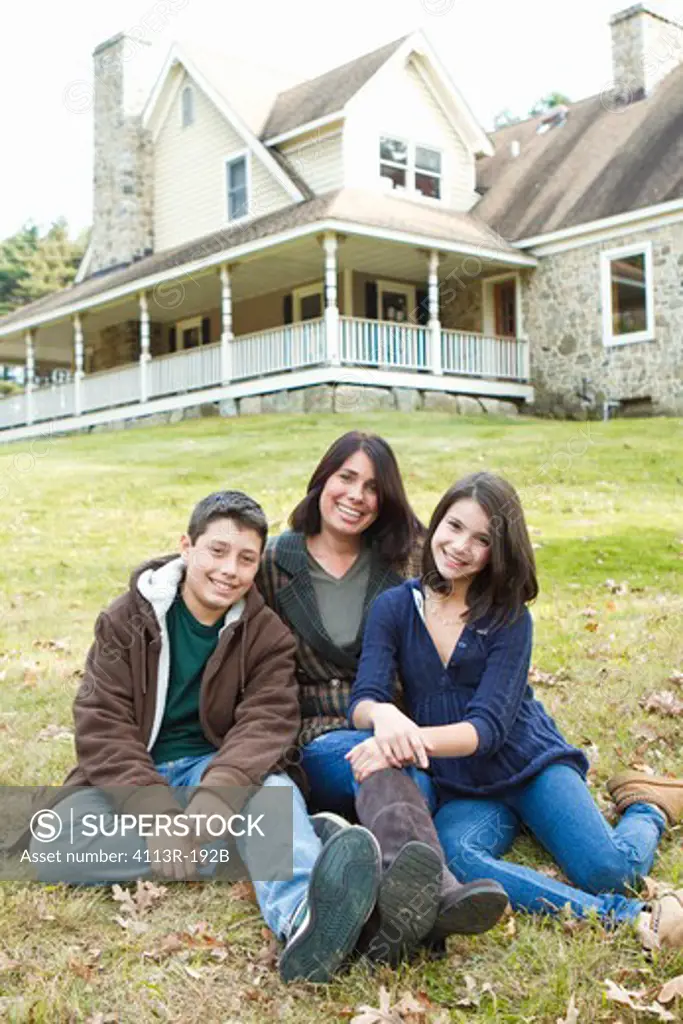 Portrait of smiling mother with two children sitting in front of large house