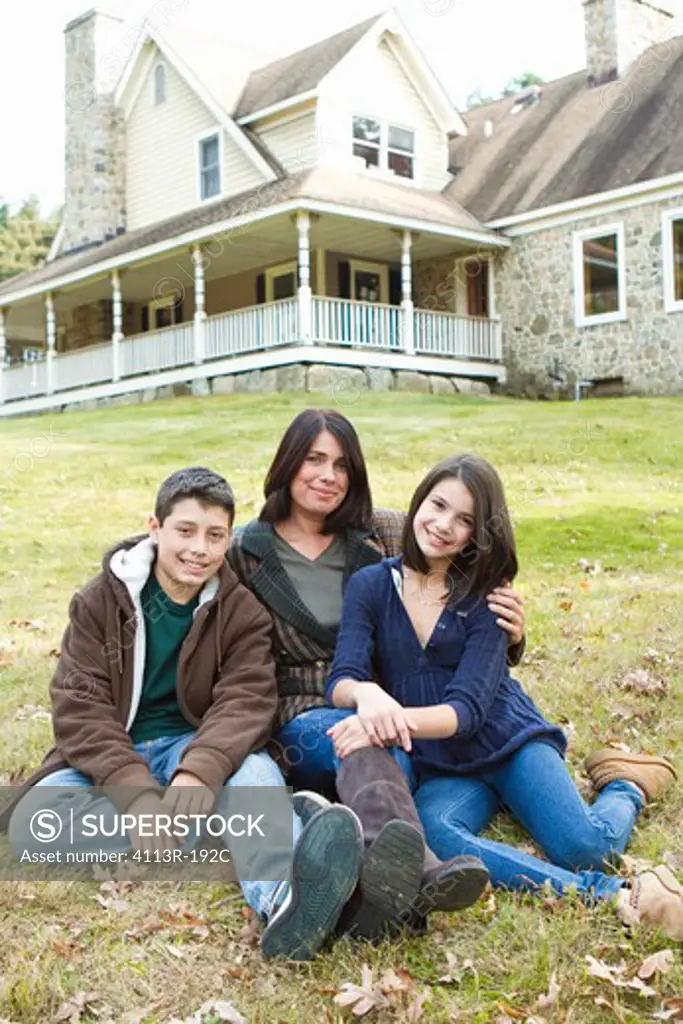 Portrait of smiling mother with two children sitting in front of large house