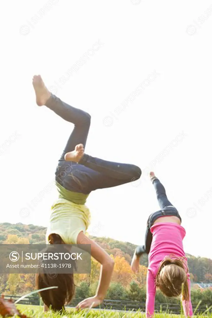Two girls doing handstand in field