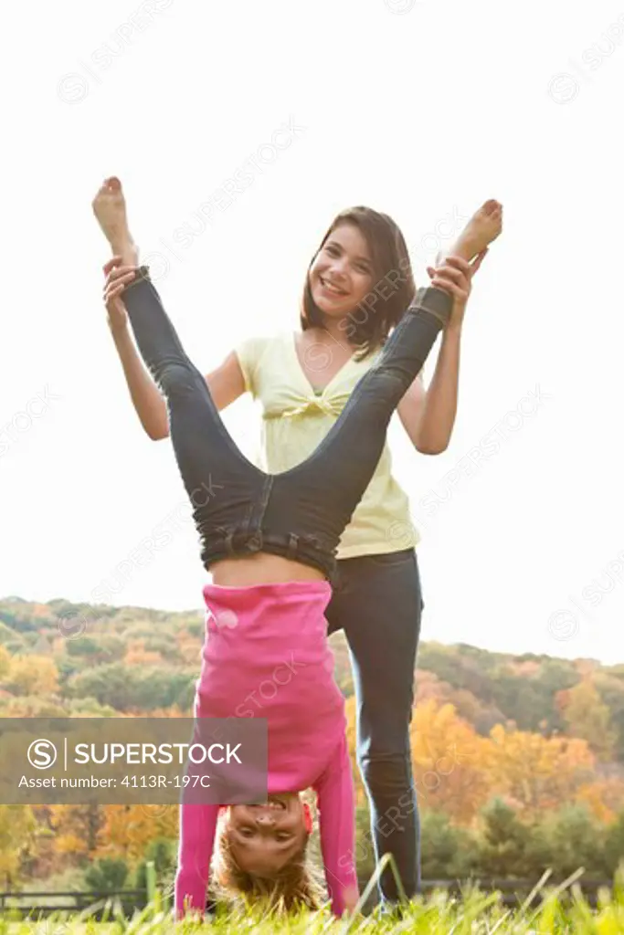 Girls helping friend doing handstand in field