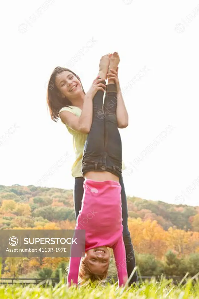 Girls helping friend doing handstand in field