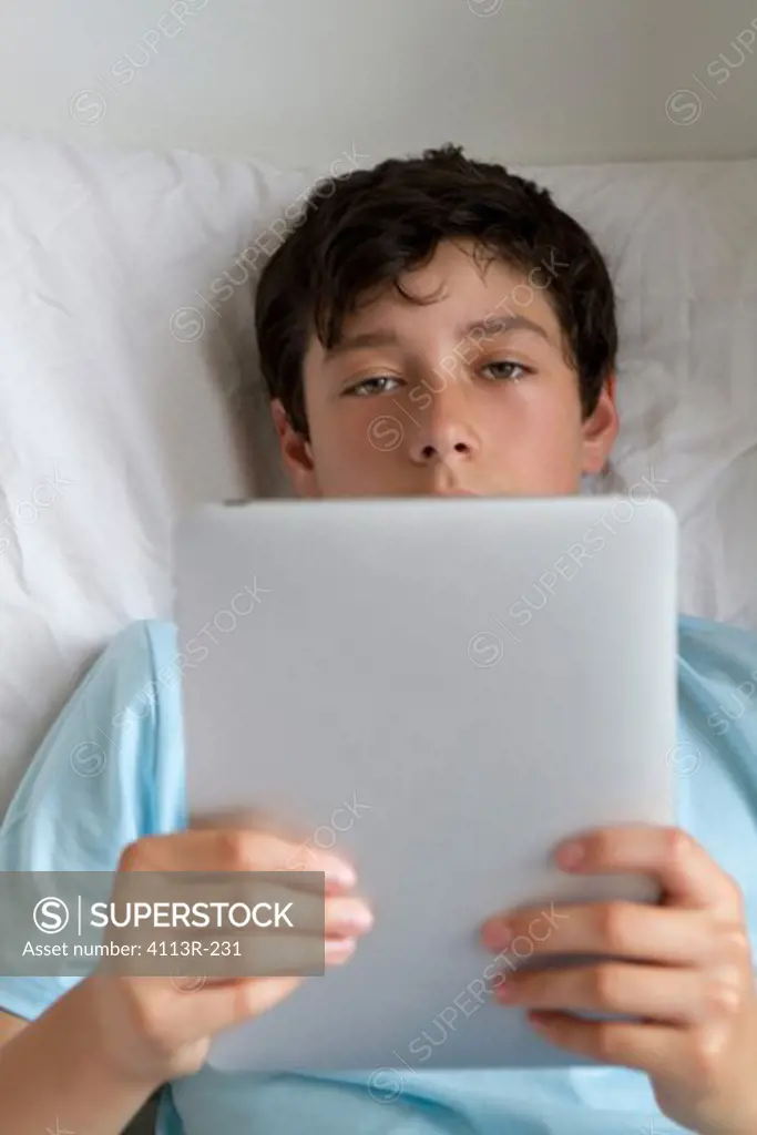 Boy lying in bed holding tablet pc