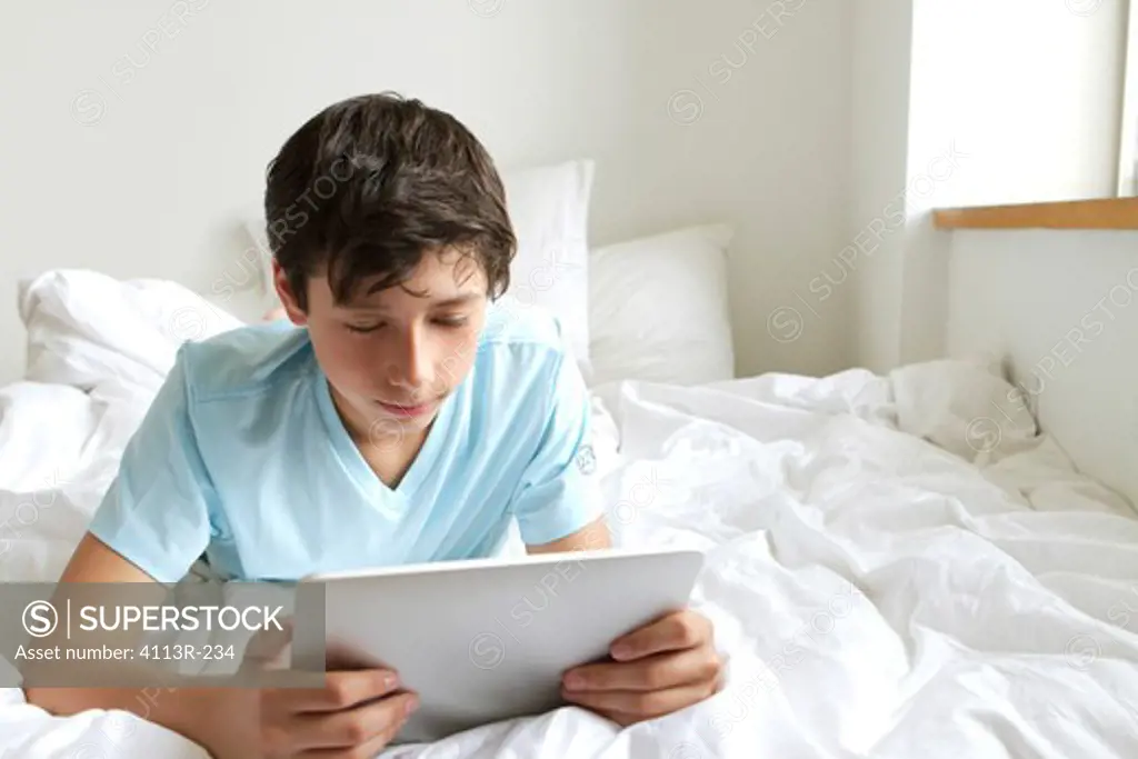 USA, New York City, Manhattan, Boy lying on bed using tablet pc