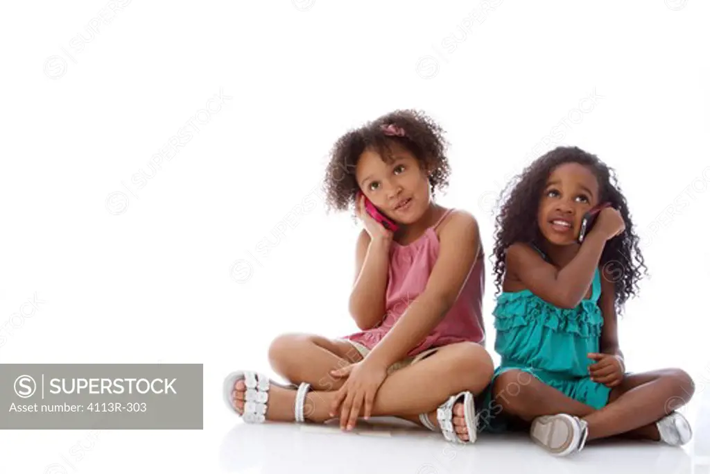 Studio shot of two girls sitting and talking on mobile phones