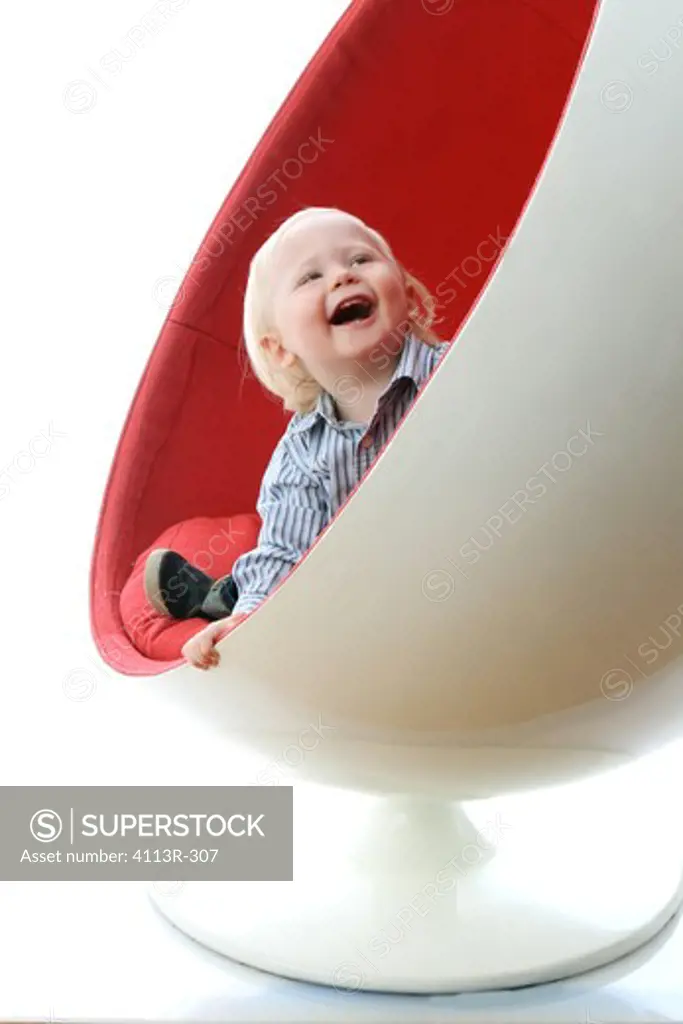 Studio shot of boy seating in red and white chair