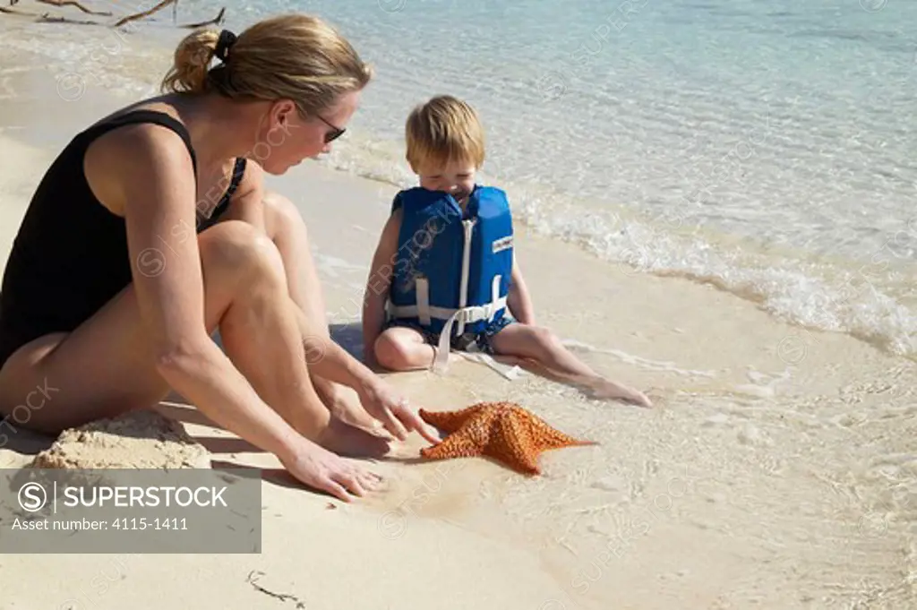 Mother and child with a starfish on the beach, Bahamas, Caribbean.