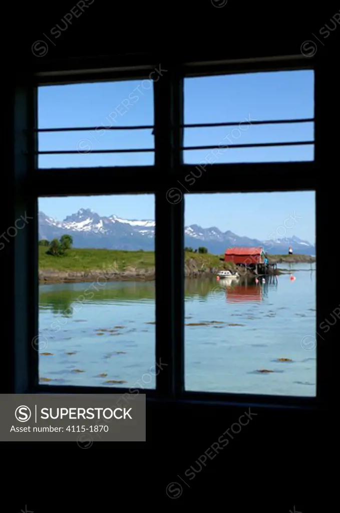Still waters and snow capped mountains of the Lofoten Islands, as seen through a window on land.