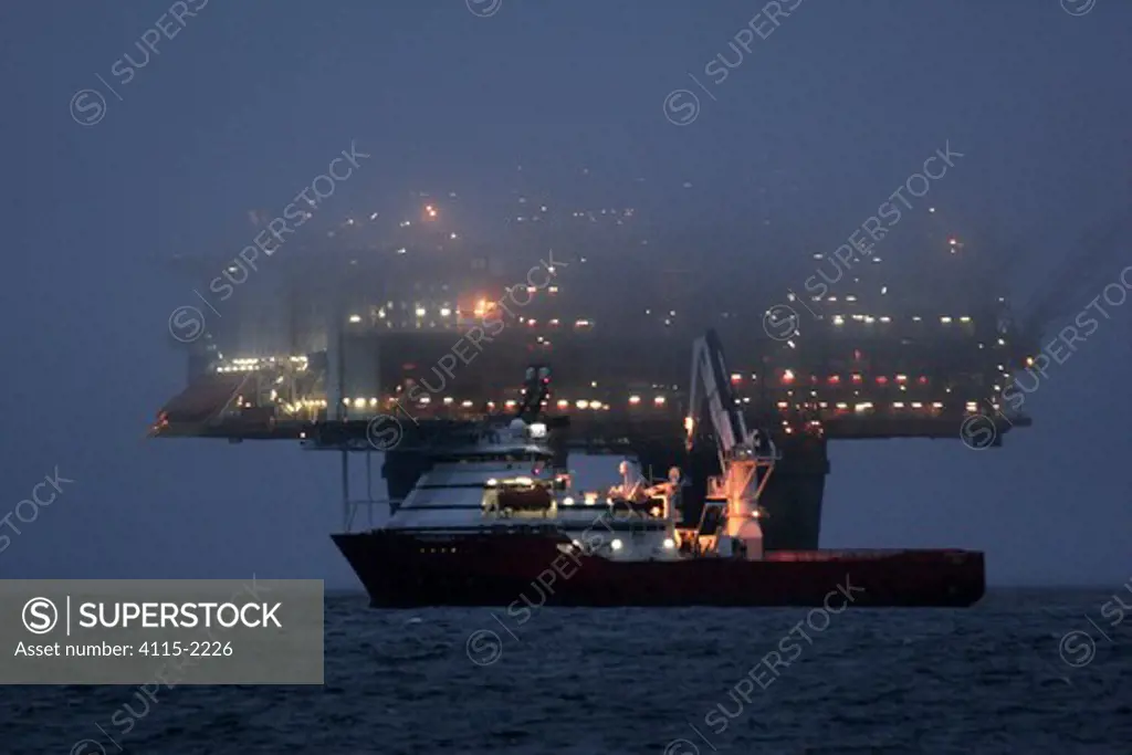 The Statfjord Bravo production platform at dusk shrouded in mist with the dive support vessel Skandi Carla undertaking subsea operations in front, North Sea, September 2006