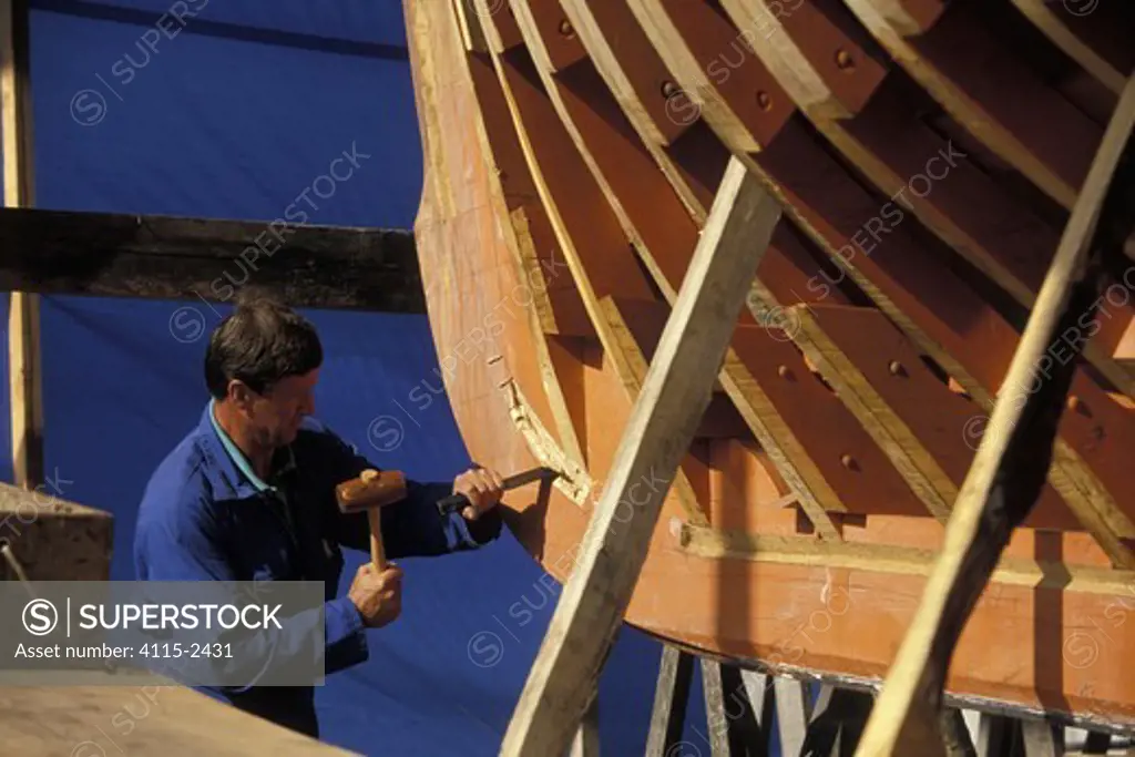 Shipwright hammering a chisel into the hull of replica tuna boat 'Marche Avec' during construction at Concarneau boatyard, Brittany, France. 1992.
