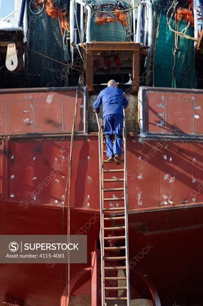 Man climbing ladder to trawler in the boatyard at Guilvinec. Finistere, Brittany, France, October 2010. For editorial use only.