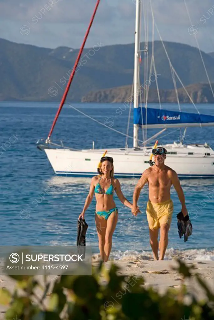 Couple with snorkelling gear emerging from the water near a Sunsail Oceanis 523 at anchored in the BVI's. March 2006. Model and property released.