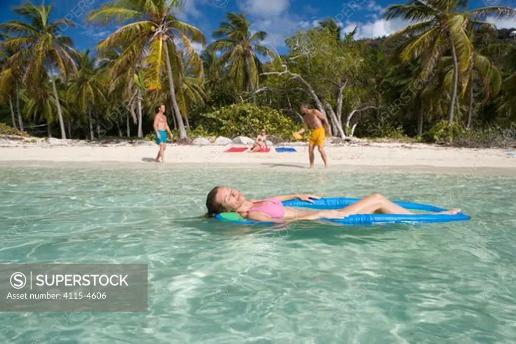 Woman relaxing on a lilo, floating off the coast of the BVI, with two men playing frisbee. April 2006, Model released.