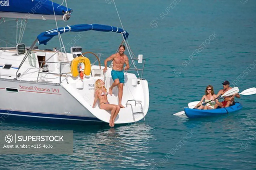 Couple relaxing on the stern of a Sunsail yacht in the British Virgin Islands, with friends kayaking. March 2006, Model and property released.