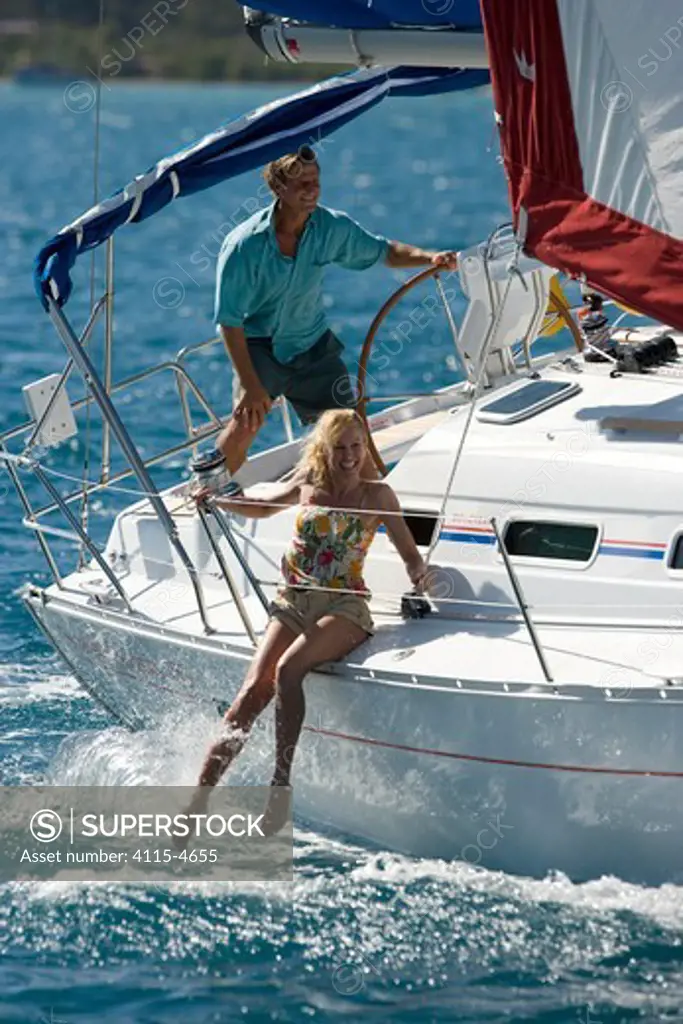 Woman dangling her legs over the side of a Sunsail yacht sailing in the British Virgin Islands, March 2006. Model and property released.
