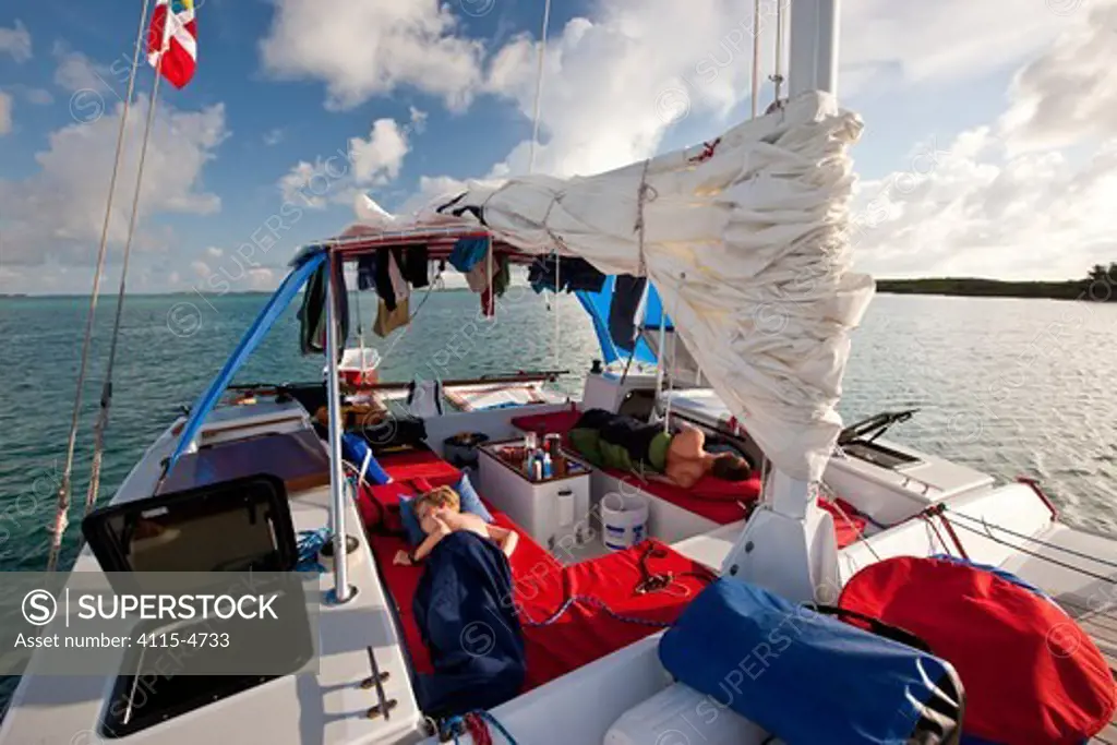 Boys sleeping on deck of 30ft Tiki catamaran 'Abaco' anchored in the Exumas, Bahamas, Caribbean. June 2009. Model and property released.
