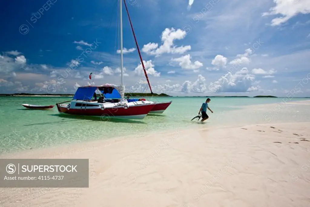 Young man dragging 30ft Tiki catamaran 'Abaco' closer to the shore. Exumas, Bahamas, Caribbean, June 2009. Model and property released.