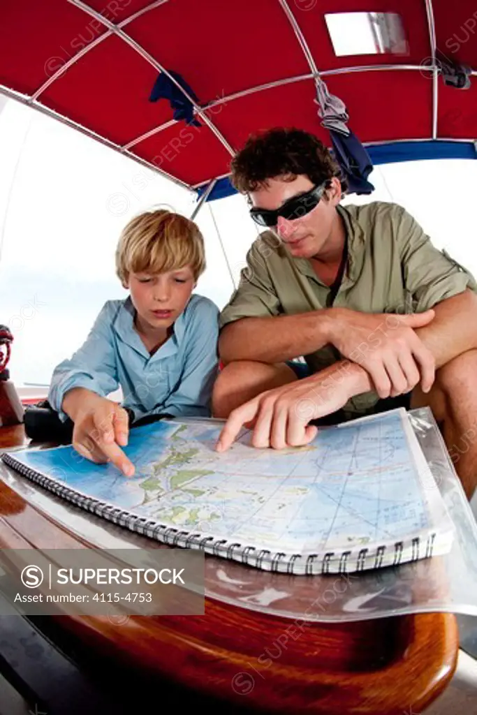 Boy and young man reading a map aboard 30ft Tiki catamaran 'Abaco'. Exumas, Bahamas, Caribbean. June 2009, Model and property released.