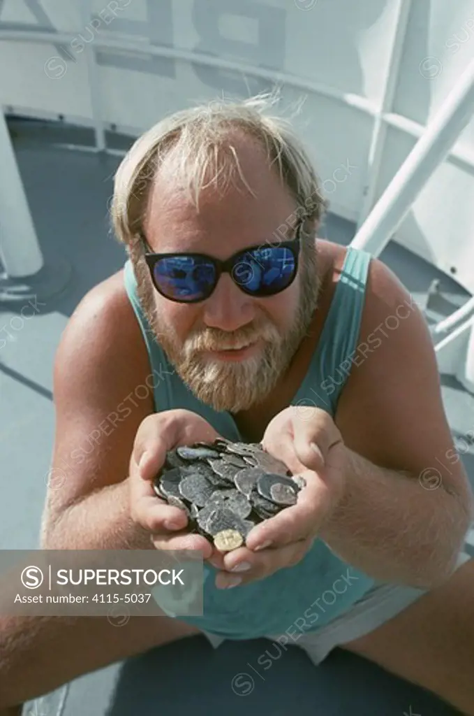 Man holds up gold and silver Doubloons recovered from the shipwreck ""Las Maravillas"", a Spanish galleon sunk in 1658, Bahamas. 1987