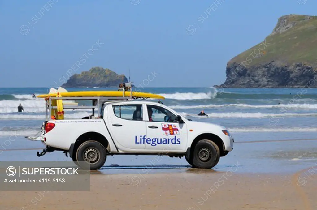 RNLI surf lifeguard driving rescue car on Polzeath beach, with surfers in waves behind. Cornwall, UK, April 2010.