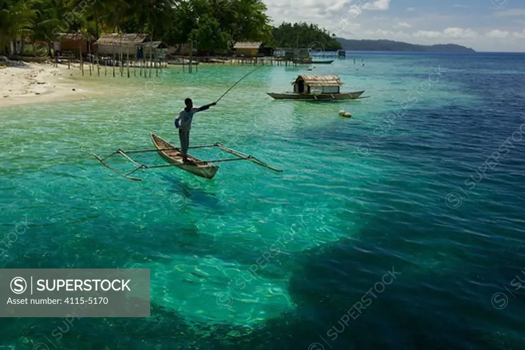 View of beach, and man fishing from a dugout canoe, at Yenbeser Village. Alfred Russel Wallace based himself in this village for several months in the 1850's. Raja Ampat Islands, Indonesia. May 2007