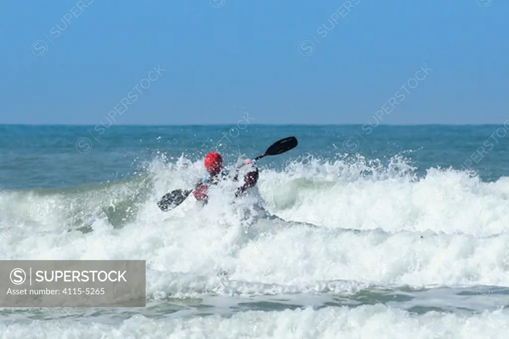 Surf kayaker paddling out through breaking waves on Polzeath beach. Cornwall, UK, April 2010.