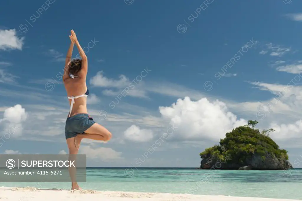 Young woman in ""tree"" yoga pose, looking out to sea. Daram Island, Raja Ampat, West Papua, Indonesia, January 2010