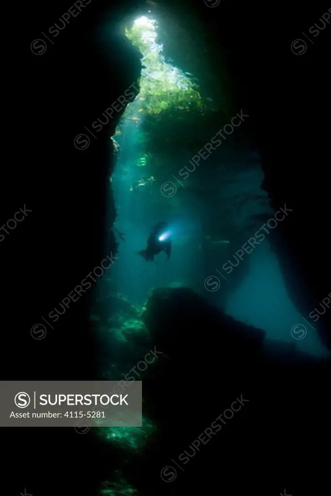 Light streaming into a shallow cave in a dive site called The Passage, with a diver swimming through. North Raja Ampat, West Papua, Indonesia, February 2010