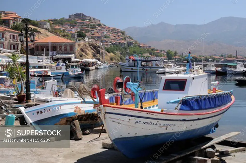Wooden fishing boats on quayside awaiting repair and maintenance at Molyvos / Mithymna harbour with town and 13th century castle on the hill in the background. Lesbos / Lesvos, Greece, August 2010