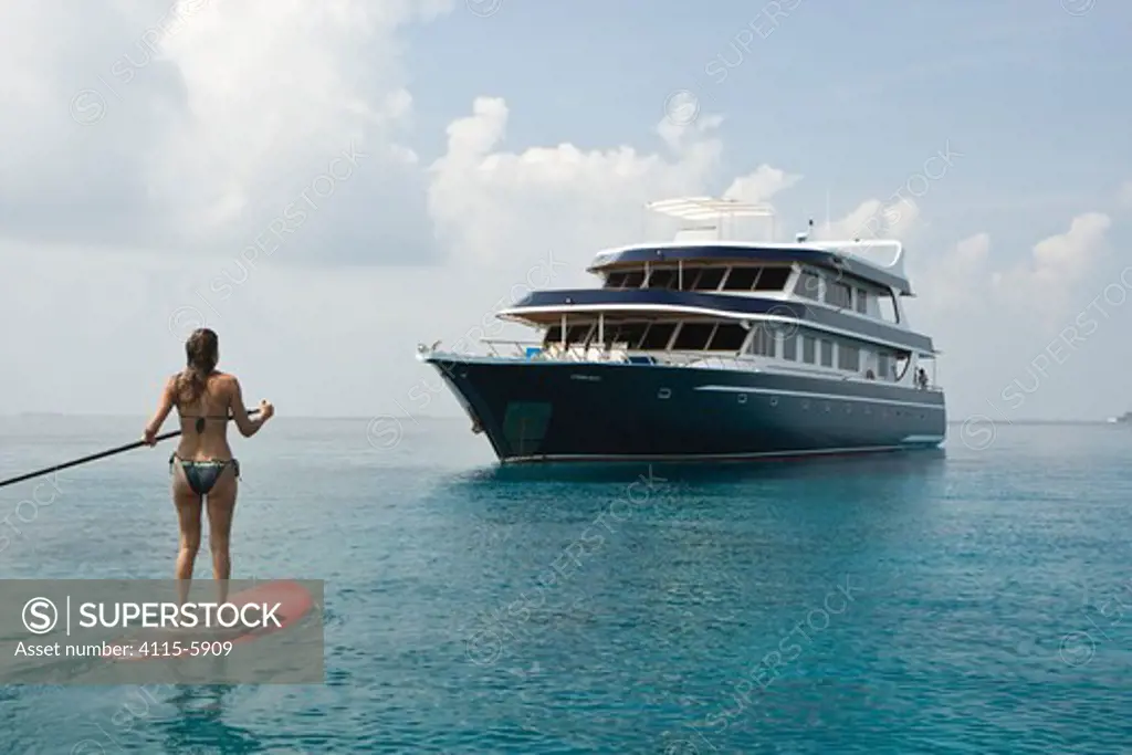 Woman paddle boarding in the Maldives with the PR liveaboard dive boat Ocean Dancer in the background. November 2008. Model and property released.