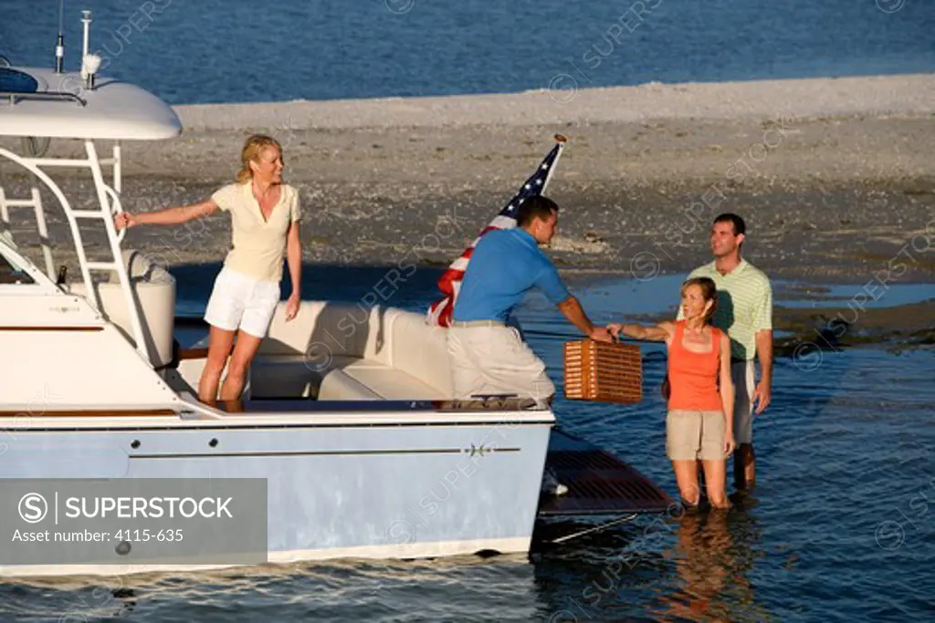 Man passing a picnic basket from the stern of Surf Hunter 33 to a couple in the shallows, Marco Island, Florida, USA