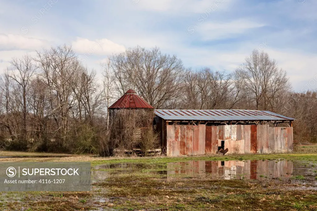 USA, Arkansas, Rusty barn and silos by pool of water in field