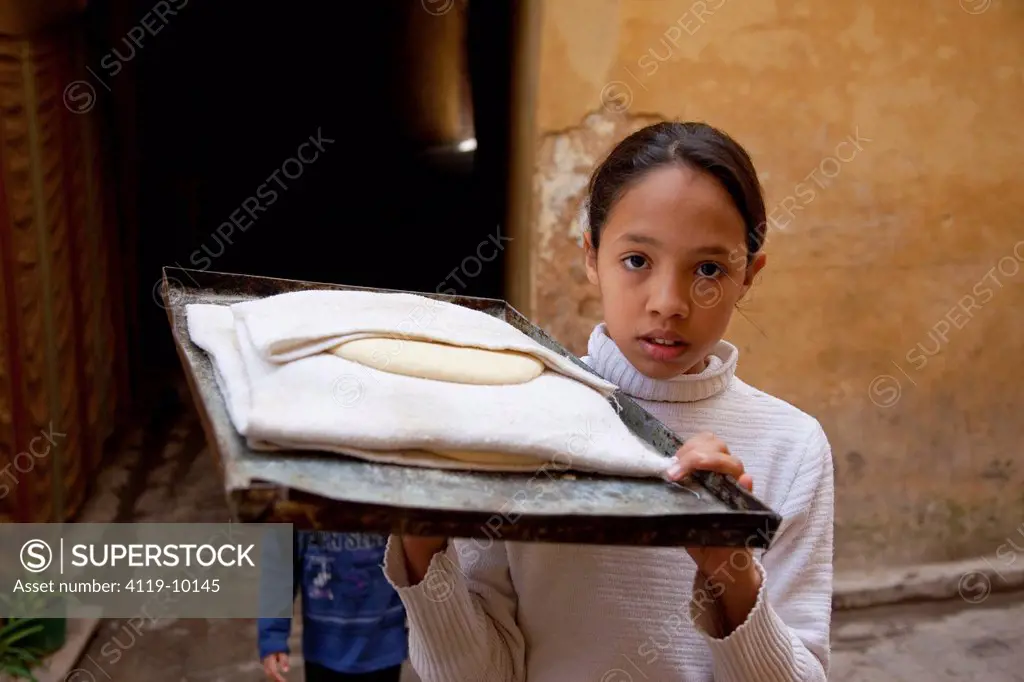 Photograph of Moroccan girl with a big tray of dough ready to be baked to bread in the streets of the Moroccan city of Fes