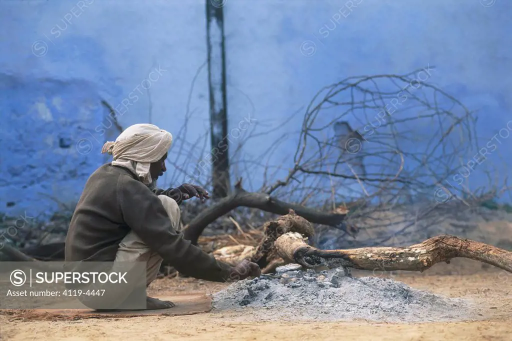 Photograph of an Indian man sitting infront of a bonfire